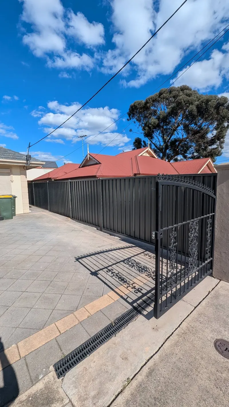Colorbond fence and wrought iron gate on a paved driveway