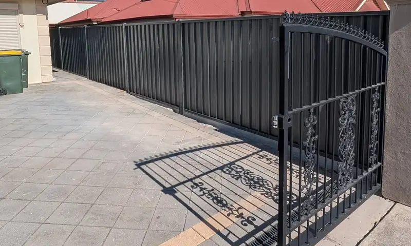 Colorbond fence and wrought iron gate on a paved driveway